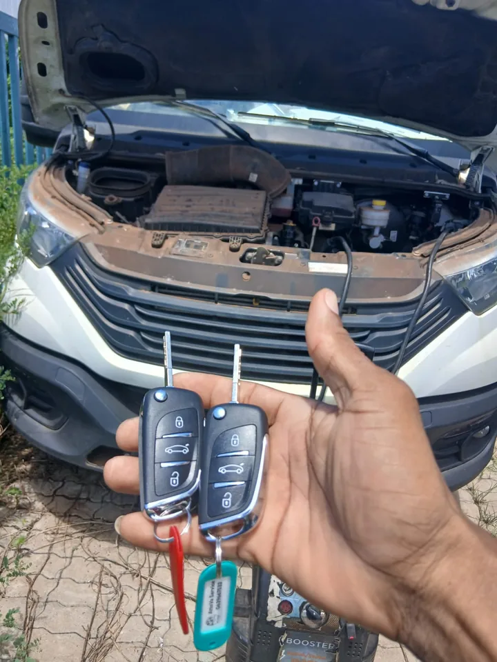 Deux clés à télécommande présentées devant un véhicule Peugeot, capot ouvert. — AttoVa Service, Mayotte.
