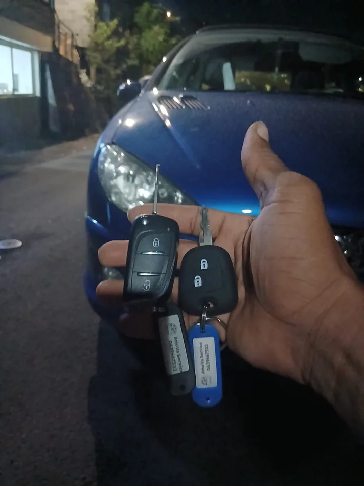 Une clé et une télécommande présentées devant un véhicule Peugeot bleu. — AttoVa Service, Mayotte.